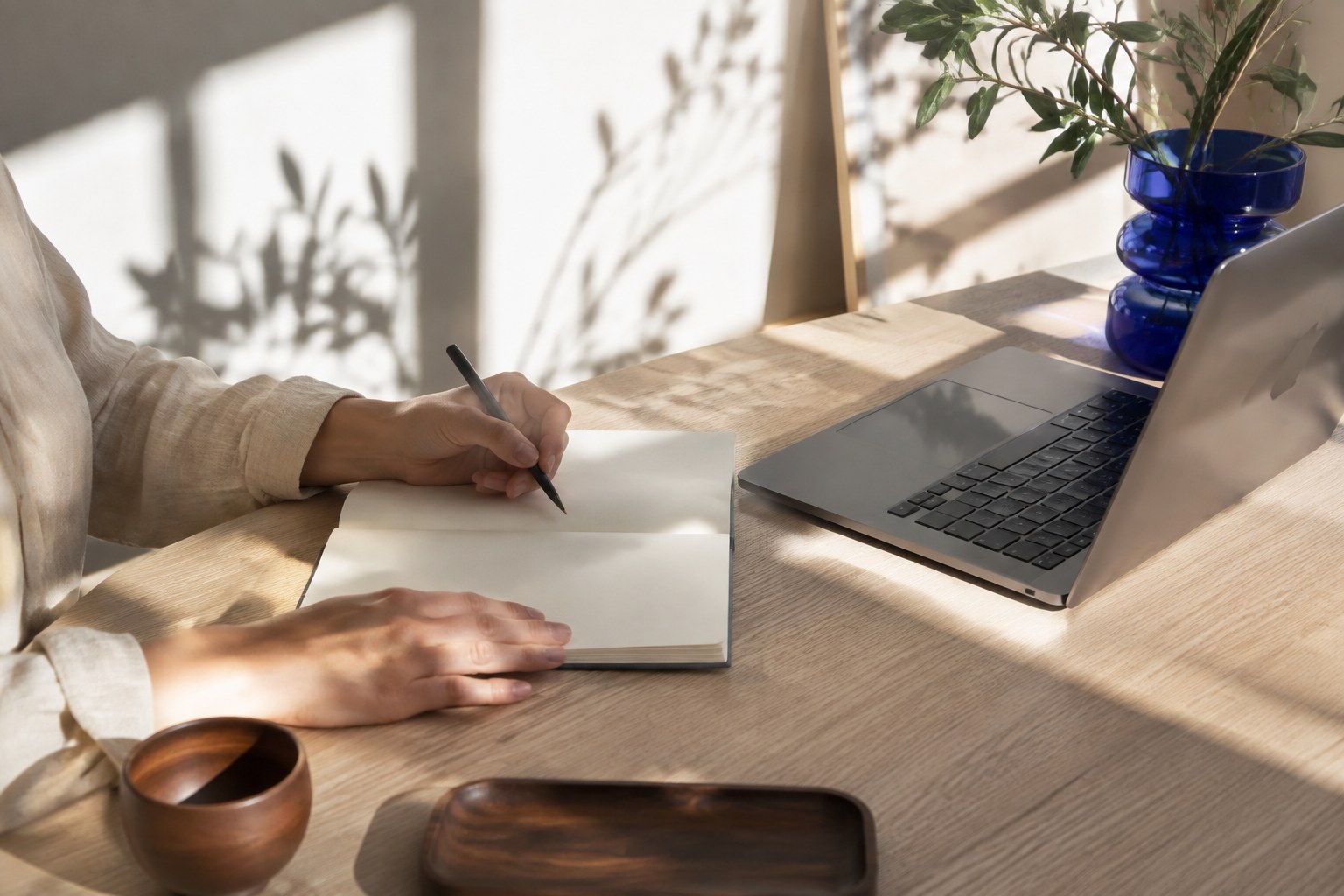 A person writing in a notebook beside an open laptop, in natural light